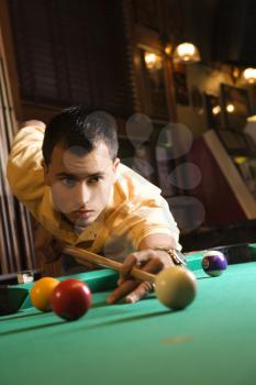 Young man concentrating while aiming at pool ball while playing billiards.