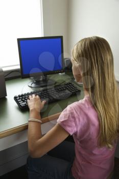 Caucasian pre-teen girl using computer and looking at monitor.