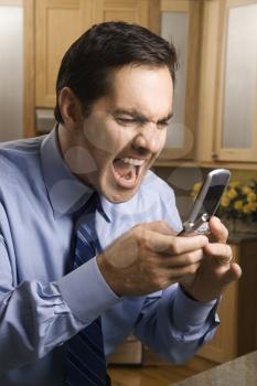 Mid-adult Caucasian male screaming at cell phone while standing in kitchen.