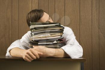 Mid-adult Caucasian male resting head on stack of paperwork.