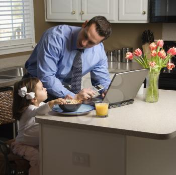 Royalty Free Photo of a Father Using a Laptop With His Daughter Eating Breakfast Beside Him