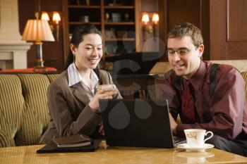 Royalty Free Photo of a Businessman and Businesswoman Drinking Coffee and Looking at  a Laptop