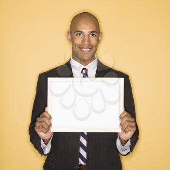 Royalty Free Photo of a Man Smiling Holding a Blank Sign Against a Yellow Background