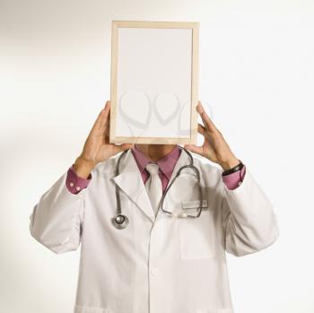 Asian American male doctor holding blank sign over face.