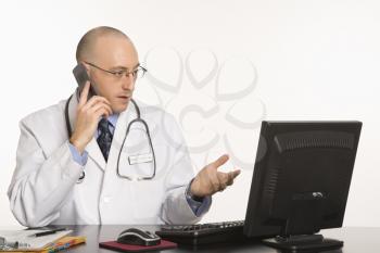 Royalty Free Photo of a Physician Sitting at a Desk With a Computer, Talking on a Cellphone