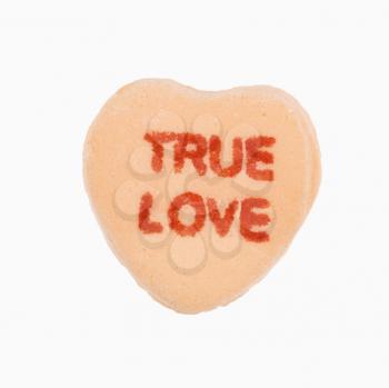 Orange candy heart that reads true love against white background.