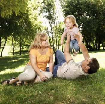 Royalty Free Photo of Parents Holding Their Toddler Daughter in the Air Playing at a Grassy Park