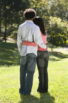 Royalty Free Photo of a Rear View of a Couple Standing in a Park With Arms Around Each Other