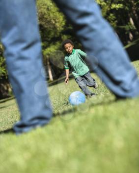 Royalty Free Photo of a Son running and kicking ball towards father in park