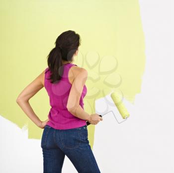Royalty Free Photo of a Woman Standing and Looking at a Partially Painted Wall Holding a Paint Roller