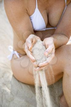 Royalty Free Photo of
a Woman Sitting on a Beach Sifting Sand Through Her Fingers