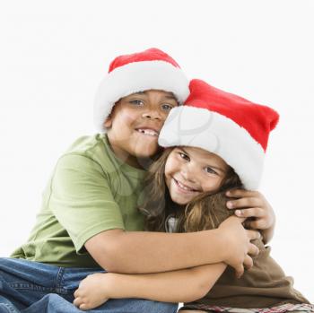 Royalty Free Photo of a Brother and Sister Wearing Santa Hats Hugging