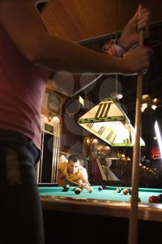 Young man lines up a pool shot with his competitor in the foreground. Vertical shot.