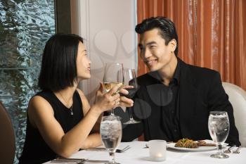Attractive young Asian couple toast their wine at a restaurant table. Horizontal shot.