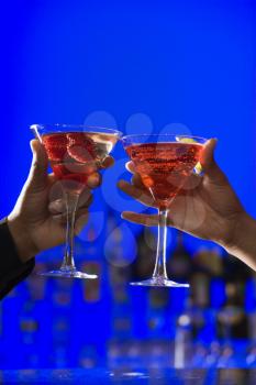 African-American hands toast martini glasses against a bright blue background. Vertical shot.