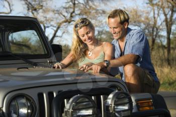 A smiling man and woman look at a map spread out on the hood of a car. Horizontal format.