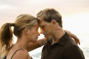 Close-up of an attractive man and woman smiling at each other with heads together, with ocean waves visible in the background. Horizontal format.
