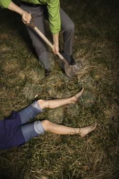 Businessman digs into the ground with a shovel to bury a womans body. Vertical shot.
