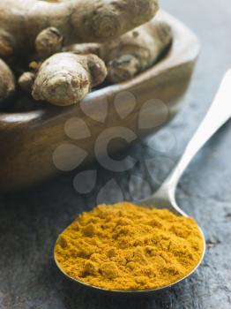 Royalty Free Photo of a Spoon of Turmeric Powder With Fresh Turmeric Root