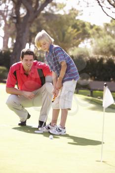 Father Teaching Son To Play Golf On Putting On Green