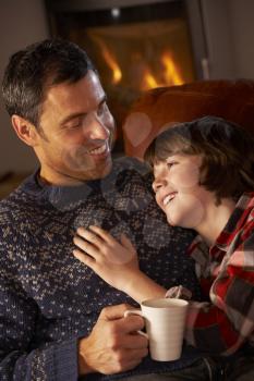 Father And Son Relaxing With Hot Drink By Cosy Log Fire