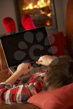 Young Boy Relaxing With Laptop By Cosy Log Fire