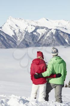 Couple Admiring Mountain View Whilst On Ski Holiday In Mountains