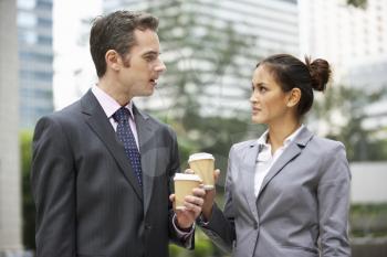 Businessman And Businesswoman Chatting In Street Holding Takeaway Coffee