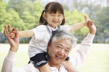 Chinese Grandfather Giving Granddaughter Ride On Shoulders In Park