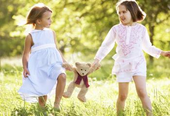 Two Young Girls Walking Through Summer Field Carrying Teddy Bear