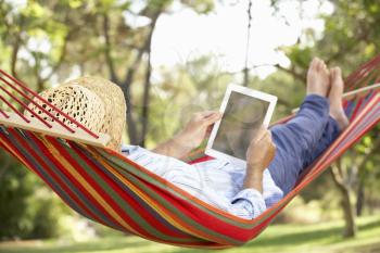 Senior Man Relaxing In Hammock With  E-Book