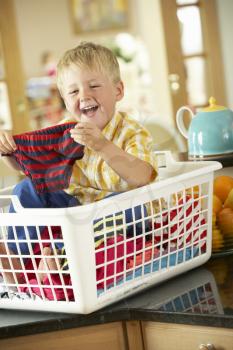 Boy Sitting In Basket Sorting Laundry On Kitchen Counter