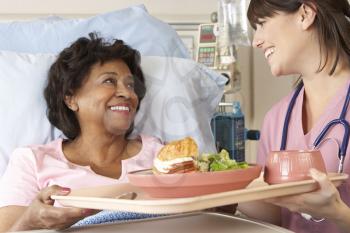Nurse Serving Senior Female Patient Meal In Hospital Bed
