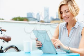 Young Woman Sitting On Roof Terrace Using Digital Tablet