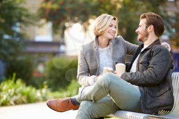 Couple Relaxing On Park Bench With Takeaway Coffee