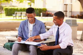 Teacher Sitting Outdoors Helping Male Student With Work