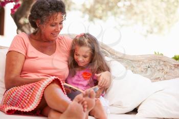 Grandmother With Granddaughter Reading Book In Garden