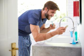 Man In Pajamas Brushing Teeth And Using Mobile Phone