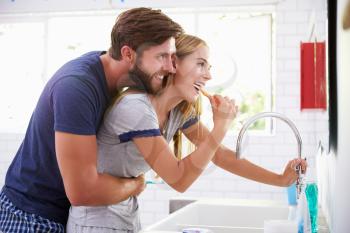 Couple In Pajamas Brushing Teeth In Bathroom