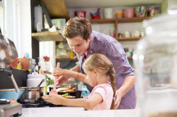 Daughter Helping Father To Cook Meal In Kitchen