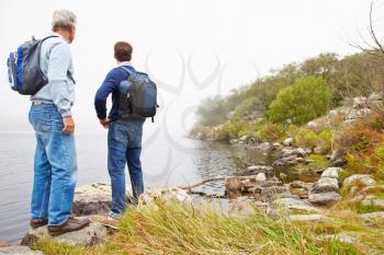 Father and young adult son standing by a lake admiring the view