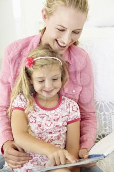 Mother And Daughter Reading Book In Bedroom