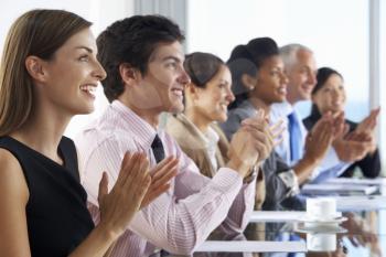 Line Of Business People Listening To Presentation Seated At Glass Boardroom Table