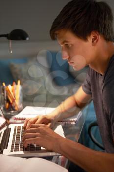 Teenage Boy Studying At Desk In Bedroom In Evening On Laptop
