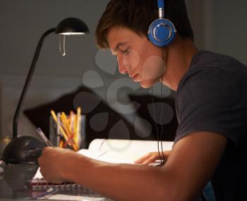 Teenage Boy Listening to Music Whilst Studying At Desk In Bedroom In Evening