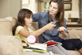 Mother Becoming Frustrated As Daughter Watches TV Whilst Doing Homework Sitting On Sofa At Home