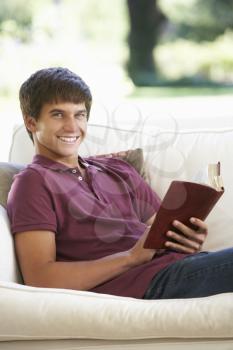 Teenage Boy Relaxing On Sofa At Home Reading Book