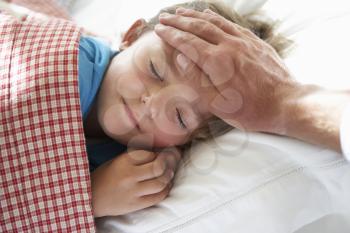 Parent Taking Temperature Of Young Boy Asleep In Bed
