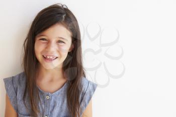 Smiling Young Girl Standing Outdoors Against White Wall