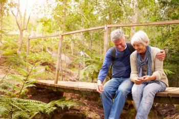 Happy senior couple sitting on bridge in forest, horizontal